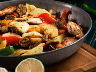 a pan filled with chicken and vegetables on a cutting board