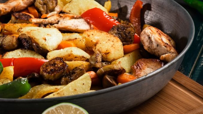 a pan filled with chicken and vegetables on a cutting board