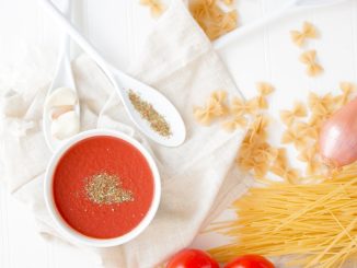 four red tomatoes beside pasta and bowl