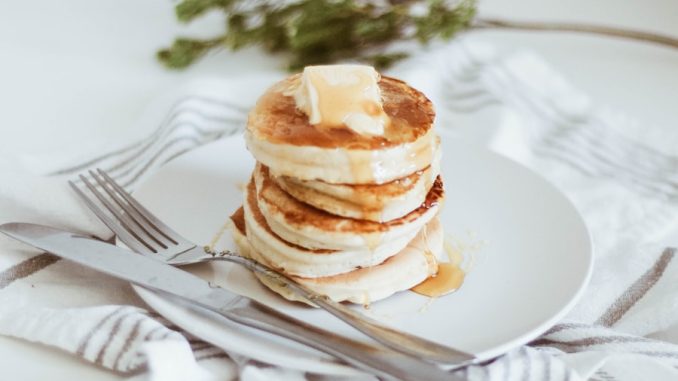 cooked pancake on round white ceramic plate beside butter knife and fork