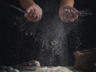 person pouring flour on table beside eggs and whisk