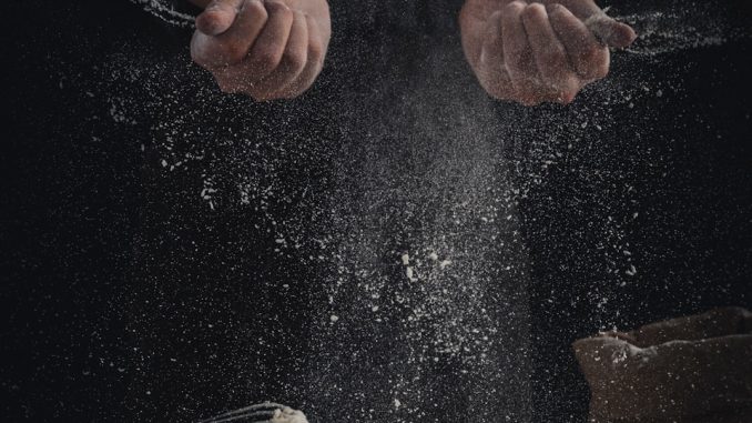 person pouring flour on table beside eggs and whisk