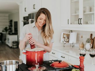 smiling woman standing and putting pepper on stock pot